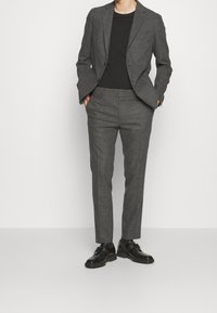 Ušitý šedý oblek s texturovaným povrchem. Blazer má klopové límce a jedno knoflíkové zapínání; kalhoty jsou slim-fit. Oblečený s černým tričkem a černými botami.