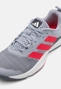 Gray athletic shoe with red accents, mesh and synthetic upper, textured surface, lace-up design, and a white sole. Black logo on tongue.