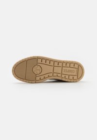 Semelle de sneaker en caoutchouc couleur tan, présentant une surface texturée avec des motifs circulaires et en zigzag, portant la marque "Cooper" près du talon.