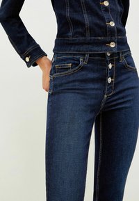 Mörkblå denimjacka och jeans har kontrasterande gula sömmar, knappdetaljer och fickor både på jackan och jeansen.