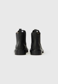 Botas de tobillo de cuero negro con paneles laterales elásticos, logotipo amarillo en contraste en la parte posterior y suelas de goma negra resistentes.