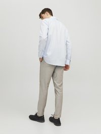 Chemise boutonnée bleu clair à manches longues, associée à un pantalon tapered gris clair et des chaussures en daim noir. Personne vue de dos.