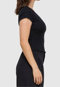 Černé přiléhavé tričko s krátkými, vykrojenými rukávy a rovním lemem. Vyrobeno z měkkého, pružného materiálu, který ukazuje jednoduchý design.