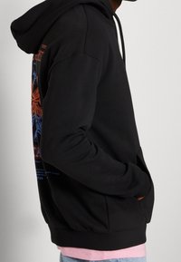 Felpa nera con cappuccio e maniche lunghe, con grafica colorata stampata sul retro. Polsini e orlo a coste, con tasca a marsupio frontale.