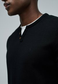 Suéter negro de punto con un diseño tipo henley, que cuenta con un cuello redondo y tres botones marrones en el collar. Tejido texturizado con un detalle sutil del logo.
