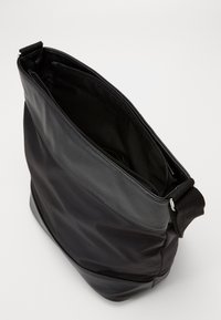 Borsa a spalla nera realizzata in tessuto testurizzato con un accentuato in pelle liscia. Presenta una chiusura superiore con zip e una tracolla regolabile in nylon.
