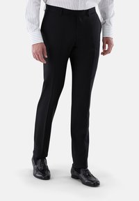 Schwarze, maßgeschneiderte Hose mit glatter Textur, klassischem Schnitt und Bügelfalte. Kombiniert mit einem gestreiften Hemd und schwarzen Schuhen.