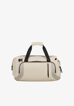 Beige Duffel-Tasche mit schwarzen Griffen, vorderer Reißverschlusstasche und strukturierten Eckakzenten auf weißem Hintergrund.