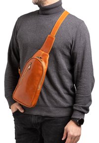 Borsa a tracolla in pelle arancione con una superficie liscia, che presenta una silhouette curvata e una tasca con zip. Indossata in diagonale sul corpo.