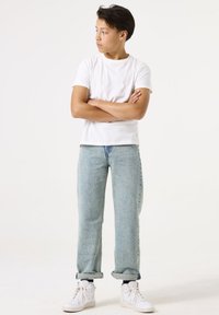 Camiseta blanca de algodón, jeans claros de corte holgado, puños doblados y zapatillas deportivas altas blancas. Un conjunto simple y casual sin estampados.