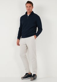 Navy zip-up sweater in a ribbed texture, paired with light beige trousers and dark sneakers featuring gray accents. Clean, modern design.