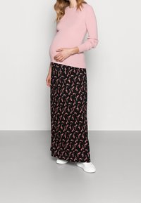 Ljusrosa ribbat långärmat tröja kombinerat med en svart blommig mönstrad maxikjol och vita sneakers, som framhäver en rundad mage.