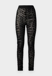 Melnie legingi ar caurspīdīgu materiālu, kas rotāts ar atkārtotu melnu "Versace Couture" teksta rakstu un ar vienkāršu melnu jostu.