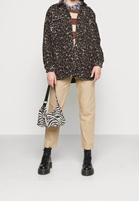 Veste chemise à imprimé léopard, haut rayé, pantalon beige et bottes noires à lacets. Sac à main à imprimé zèbre avec une bandoulière réglable.