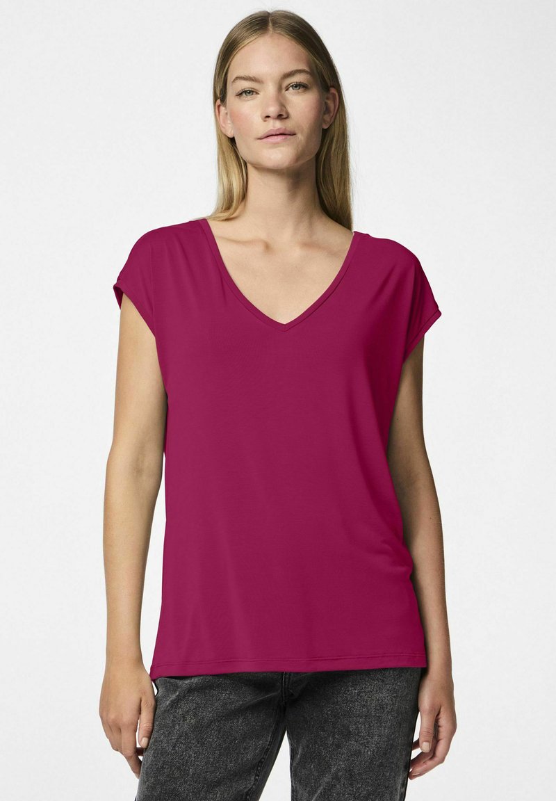 Fuksjowa koszulka z dekoltem V i krótkimi podwiniętymi rękawami, o gładkiej fakturze i luźnym kroju. Noszona z ciemnoszarymi dżinsami.