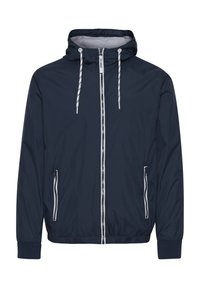 Chaqueta cortavientos de color marino, hecha de material ligero, con capucha, cordones, cremallera frontal y dos bolsillos laterales con acentos blancos.