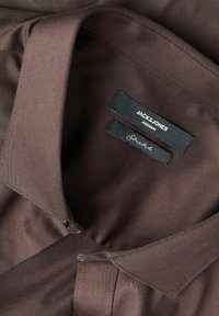 Кафява риза с якичка и гладка текстура. Етикетите гласят "JACK & JONES Premium" и "Structure" и са разположени във вътрешната страна на яка.