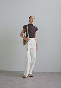 Brown fitted top, white high-waisted wide-leg pants, beige and white shoes, tan handbag with a long strap, neutral background.