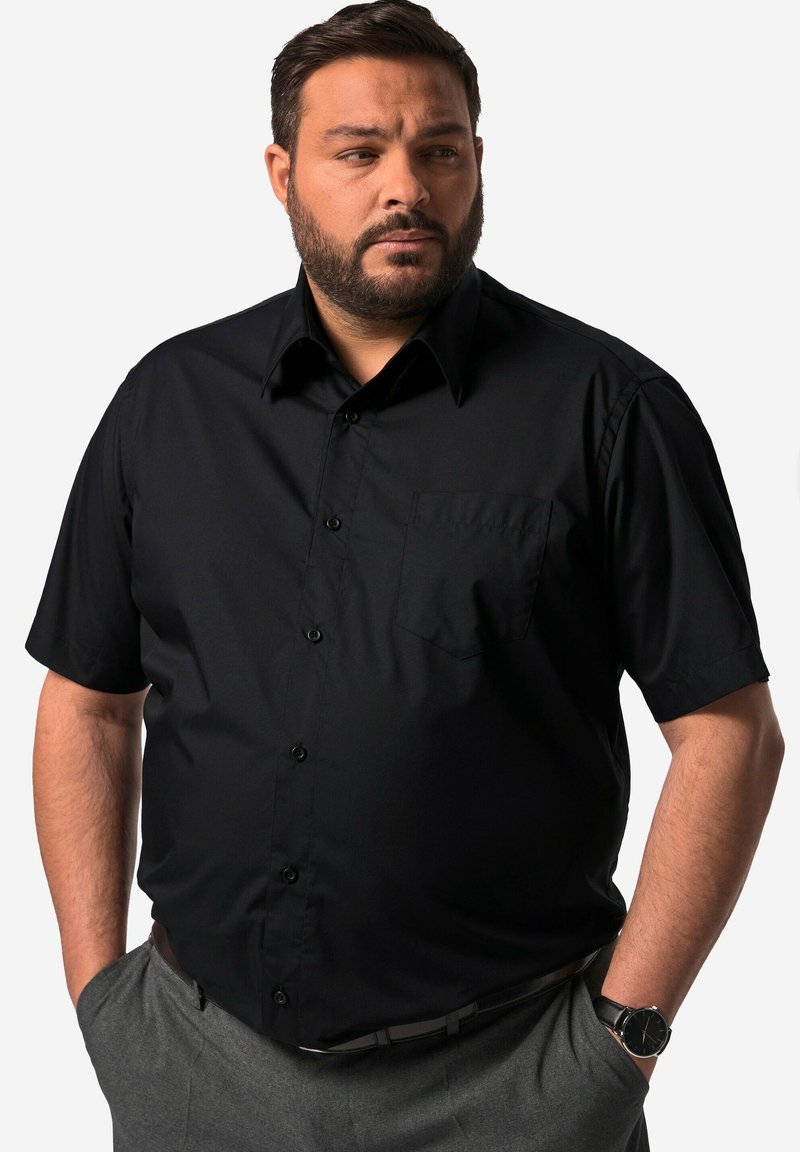 Kortärmad svart skjorta i slätt tyg, med knappframsida och bröstficka. Bärs med grå byxor och en klocka.