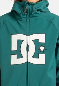 Aquagroene ritsjack met groot wit DC-logo aan de voorkant en verstelbare trekkoorden op de capuchon.