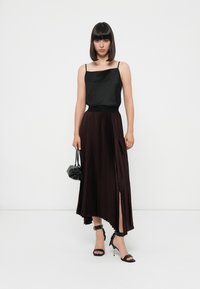 Camisola di raso nera abbinata a una gonna maxi plissettata bordeaux con spacco alto. Tacchi neri con cinturini e una piccola borsa nera completano il look.