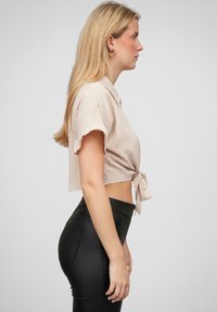 Maglietta cropped beige chiaro con maniche corte e un nodo in vita, abbinata a leggings neri a vita alta. Tessuto liscio, design casual.
