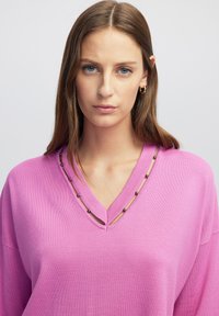 Roze v-hals trui met een relaxte pasvorm, voorzien van kraalaccenten langs de halslijn en een gladde textuur.