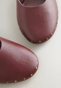 Zoccoli in pelle bordeaux con punte arrotondate, caratterizzati da una texture liscia e dettagli in metallo dorato lungo i bordi.