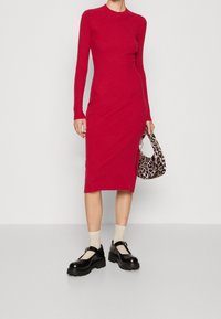 Robe rouge à manches longues côtelée avec fente latérale, associée à un sac imprimé léopard et des chaussures à plateforme noires, portées avec des chaussettes beiges.