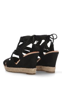 Sandalias de cuña de ante negro con diseños troquelados, lazos en el tobillo y un tacón de yute trenzado. Punta abierta y forma contorneada del tacón.