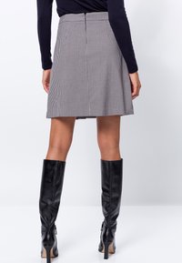 Jupe à carreaux noir et blanc avec un design évasé, comportant une fermeture éclair au dos et des poches, assortie à des bottes en cuir noir jusqu'aux genoux.
