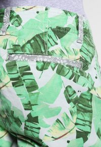 Zielone i jasnoszare spodnie w wzór, z motywem liści, z tylną kieszenią i kontrastującymi szwami. Miękka faktura materiału.