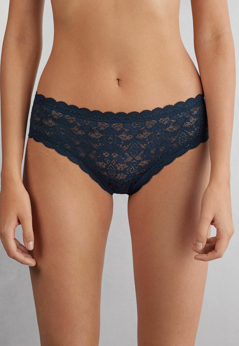 Donker marineblauwe kant slip met geschulpte randen, voorzien van bloemen- en diamantenpatronen. Zachte, doorzichtige textuur met een laag uitgesneden pasvorm.