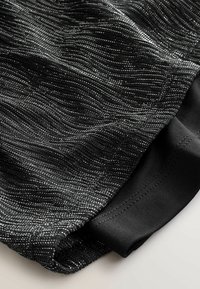 Material texturat negru cu un model în valuri, având fire metalice. Margine netedă neagră și detalii de cusătură de-a lungul marginii.