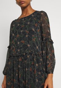 Svart blommig blus med genomskinliga långärmar, volangdetaljer och grön bakgrund. Har blommönster i vita och rostiga nyanser.