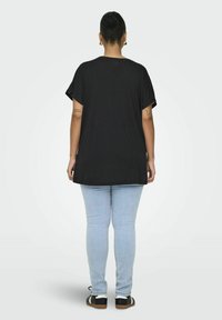 T-shirt negra oversized de manga corta, combinada con unos jeans skinny de color azul claro y zapatos negros con detalles en blanco.