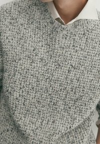 Pull en tricot gris avec un motif texturé, doté d'un col en V et d'une chemise blanche à col superposée en dessous.