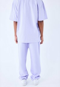 T-shirt oversize lilla e pantaloni abbinati in tessuto morbido, con sneakers bianche visibili nella parte inferiore, per un look rilassato.