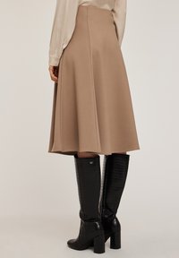 Una gonna beige con silhouette fluida e cuciture laterali, abbinata a stivali neri al ginocchio con texture coccodrillo e tacco a blocco.