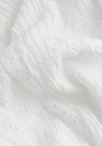 Tejido blanco texturizado con patrones de punto en forma de diamante elevado y rayas, que muestran suaves pliegues y detalles de costura intrincados.