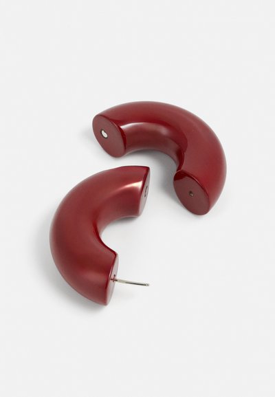 Pendientes curvos rojos, hechos de un material brillante, con un acabado pulido. Cada pendiente tiene un cierre de tuerca para un uso seguro.