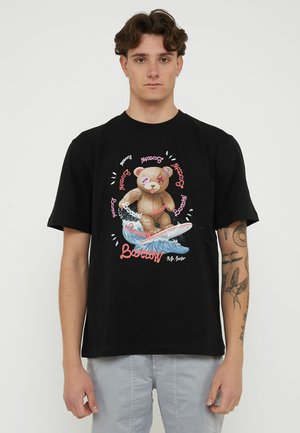 Giovane uomo che indossa una maglietta nera con la grafica di un orsacchiotto che fa surf su un'onda e diversi testi "Barrow" in rosa e bianco.