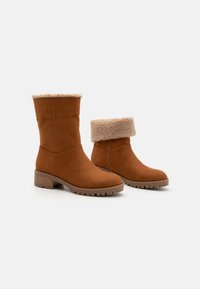 Botteurs chelsea en daim marron avec un col en velours beige, petit talon carré et semelle en caoutchouc texturé. Fini lisse avec un bout arrondi.