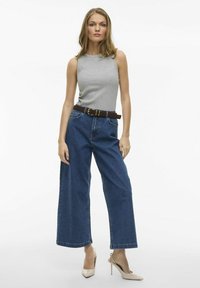 Grå ärmlös topp kombinerad med högmidjade, vida blå denimjeans. Brun bälte, beige högklackade skor. Minimalistisk design.