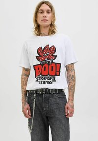 Tricou alb din bumbac cu un grafic îndrăzneț roșu și negru, având textul "Boo!" și "Stranger Things". Asortat cu blugi închisi la culoare și o curea neagră.