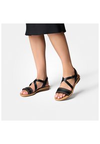 Černé kožené sandály s překříženými popruhy, šitým detailem a plochou podrážkou. Design s otevřenou špičkou, který ukazuje přirozenou barvu nehtů na nohou.