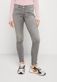 Gray skinny jeans featuring five pockets, a button closure, and subtle whiskering. Paired with multicolored athletic sneakers.