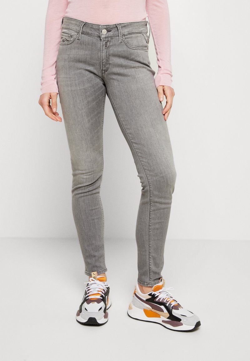 Gray skinny jeans featuring five pockets, a button closure, and subtle whiskering. Paired with multicolored athletic sneakers.