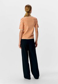 Top corto a maniche corte a righe arancioni e beige con scollatura tonda, abbinato a pantaloni neri a vestibilità ampia, visto da dietro.
