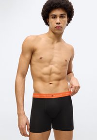 Μαύρα ανδρικά μποξέρ με πορτοκαλί ελαστική ζώνη Tommy Hilfiger, με άνετη εφαρμογή και λείο βαμβακερό υλικό, σε ανδρικό μοντέλο.